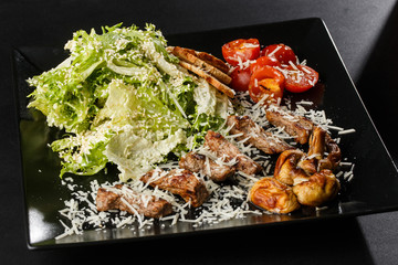 Veal salad with cherry tomatoes, mushrooms on a black plate on dark background. Plate on dark background, copy space. Restaurant food, close up. Meat salad. Horizontal photo.