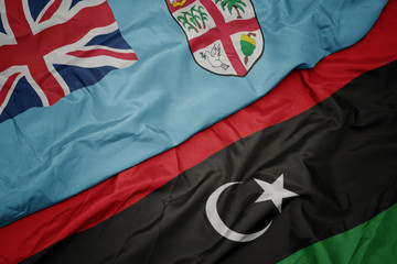 waving colorful flag of libya and national flag of Fiji .