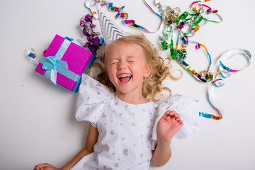 little blonde girl in birthday cap smiling with gift box and confetti on white background, little beautiful girl wearing birthday cap on isolated background smiling with happy face, space for text