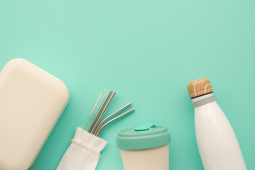 Reusable sustainable bamboo lunch box, coffee cup, metal straws, water bottle on mint background.