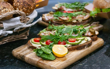 Sandwiches with tomatoes, lettuce, ham, lemon and arugula on dark bread. On wooden background