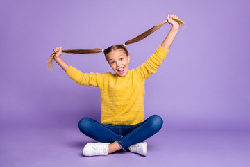 Full length photo of cheerful content child sit crossed folded legs have fun on weekends hold her ponytails wear casual style outfit isolated over violet color background