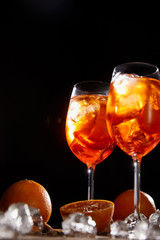 Aperol Spritz in glasses, oranges and ice cubes on black background