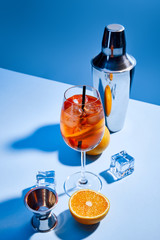 Fototapeta na wymiar cocktail Aperol Spritz, oranges, shaker, ice cubes and measuring cup on blue background