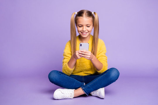 Full body photo of interested positive child sit crossed folded legs use her phone read follow blogging social media accounts wear casual style clothing isolated over violet color background