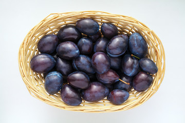 a lot of shiny ripe blue plums in a straw wicker basket