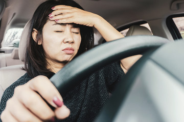 stressed Asian woman suffering from headache while driving car tired with traffic jam 