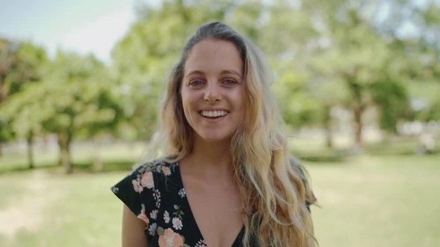 Portrait of a smiling beautiful young woman putting her hand in the blonde hair looking to camera in the park smiling 