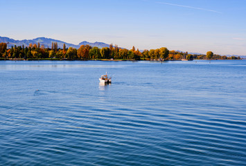 Blue lake Constance, colorful autumn trees,boat and hills.