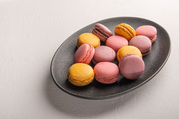 Colorful French or Italian macaron stack on dark plate put on white table with copy space