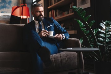 Starting new working day. Handsome man holding coffee cup sitting on the couch in office.