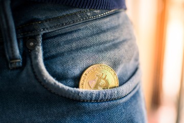 Close-up of golden metal bitcoin coin in a jeans pocket. Cryptocurrency, blockchain technology, payment and digital asset concept. 
