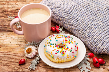 Hot coffee with a donut. Autumn drink for a good mood with plaid, fresh rose hips, leaves and flowers. Old wood plank background