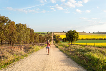 Woman walking along a dusty road among the rural fields