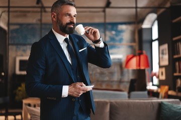 Confident man in smart casual wear holding coffee cup at his working place in office