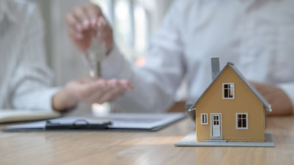Real estate agent holding a key and asking costumer for contract to buy, get insurance or loan real estate or property.