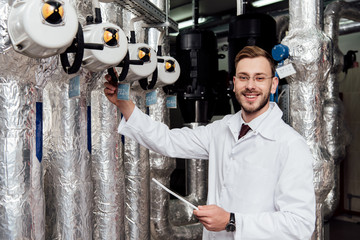 cheerful bearded engineer in white coat holding digital tablet near air supply system