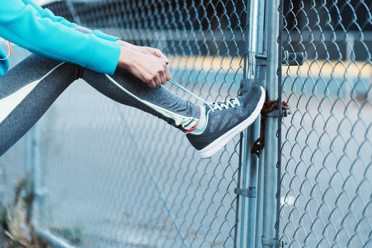 Young sporty woman tiying laces on the street before running workout