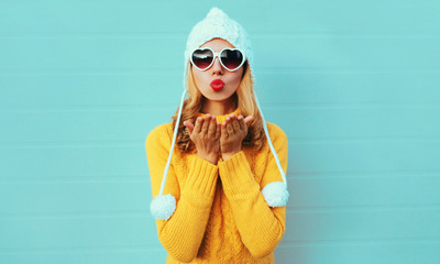 Winter portrait young woman blowing red lips sending sweet air kiss wearing yellow knitted sweater...
