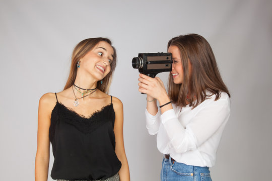 Dos chicas jugando con una c&aacute;mara de cine antigua de pel&iacute;cula de 8 mm; chicas haciendo de artistas de actriz y de directora de cine.