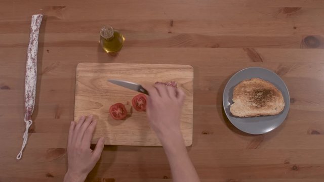 smearing bread with tomato, typical Catalan food, for breakfast, snack, dinner, accompanied by olive oil, and sausage, totally top view, only the hands are seen with a wooden bottom