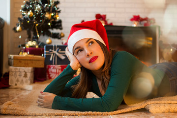 Pretty woman lying on the rug in the living room of her house with Christmas decorations and gifts in the tree.