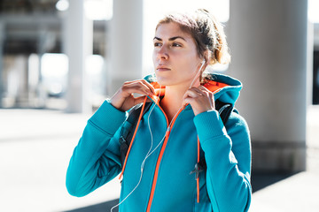Portrait of handsome fit woman listening music on the sunny street using earplugs