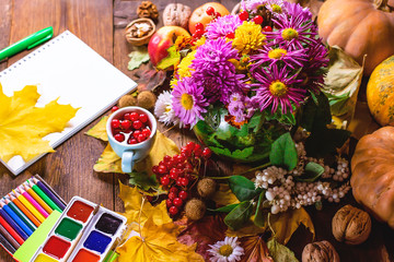 notebook and stationery, paint pencils on a background of autumn flowers and leaves