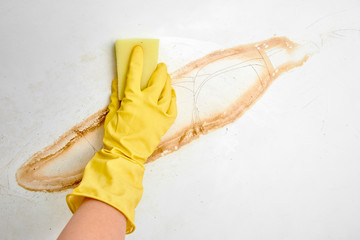 Hand in a yellow glove with a sponge washes rust with a white enamelled bath close up.