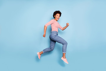 Fototapeta na wymiar Side profile full length body size photo of pretty sweet cheerful girlfriend wearing jeans denim striped shirt epxressing funny emotions jumping running isolated pastel blue color background
