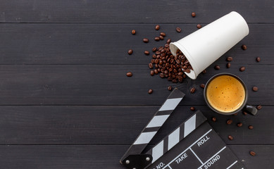 movie clapper, hot coffee and bean on black wooden background. top view