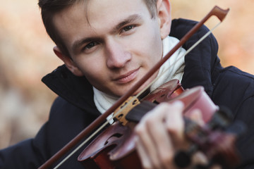 face of a young elegant man playing the violin on autumn nature backgroung, a boy with a bowed instrument practicing, musical performance outdoors, concept of hobby and art