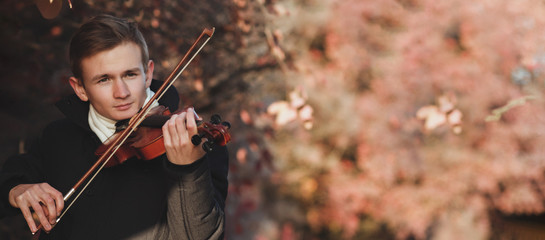 portrait of a young elegant man playing the violin on autumn nature backgroung, a boy with a bowed...