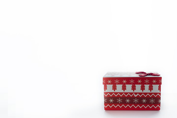 A red Christmas box with gifts and a bow stands on a white background with a place for a postcard text from the right. On the box are Christmas trees and snowflakes.