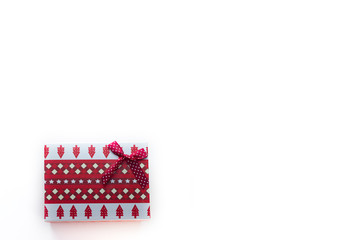 A red Christmas box with gifts and a bow stands on a white background with a place for a postcard text view from the top from the left edge. On the box are Christmas trees and snowflakes.