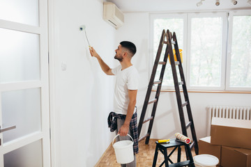 young man painting indoor wall with roller