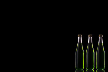 Three small glass bottles with a green drink stand on a mirror surface against a dark background...
