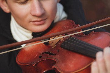 close-up portrait of a young elegant man playing the violin on autumn nature backgroung, boy's face with musical instrument under his chin, concept of hobby, art and lifestyle