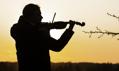 silhouette figure of a young violinist in a jacket at sunset, a man playing the violin in nature,...