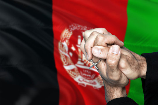 Afghanistan flag and praying patriot man with crossed hands. Holding cross, hoping and wishing.