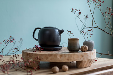 Stylish autumn composition of home decor on living room with wooden fruit tray, cement fruits, tea jug  and autumn flowers. Eucalyptus color concpet. Template. Modern decoration. Close up. 