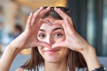 Beautiful woman looking through heart gesture made with hands