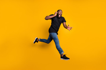 Fototapeta na wymiar Wait i hurry. Full body profile side photo of crazy funny afro american guy jump speak cellphone run buy black friday discounts wear t-shirt denim jeans isolated yellow color background