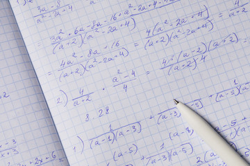 Algebraic calculations in open graph notebook with white pen. White paper with math fractions, top...