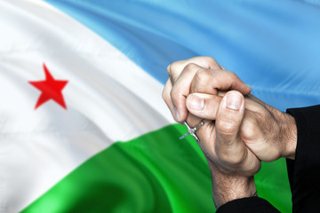Djibouti flag and praying patriot man with crossed hands. Holding cross, hoping and wishing.