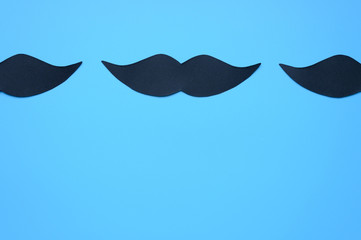 Several black paper moustache on a blue background. The concept of awareness of men's health and...
