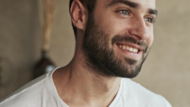 Close up view of handsome happy young brunet man smiling while looking to the side at home