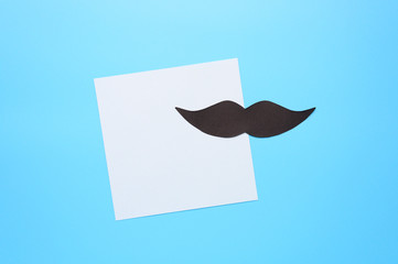 Black paper moustache and writing paper sticker on a blue background. The concept of awareness of...