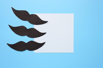 Several black paper moustache and writing paper sticker on a blue background. The concept of awareness of men's health and prostate cancer. Space for text