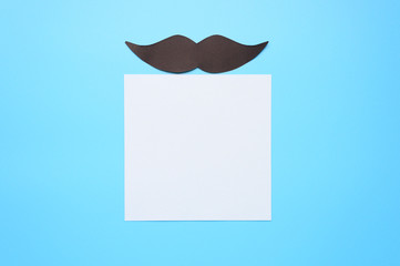 Black paper moustache and writing paper sticker on a blue background. The concept of awareness of...
